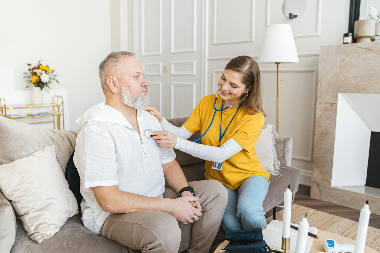 Home A nurse uses a stethoscope for a home check-up on a senior adult in a cozy living room.